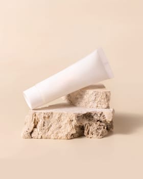 White plastic cream tube on travertine stone on light yellow, close up, mockup. Skincare beauty product. Natural cosmetics. Minimal composition..