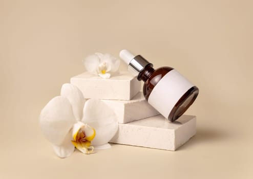Brown glass dropper bottle on stone near white orchid flowers on light yellow, close up, mockup. Skincare handmade beauty product, serum or lotion. Exotic natural cosmetics..
