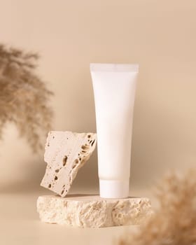 White plastic cream tube on travertine stone near dry pampas grass on light yellow, close up, mockup. Skincare beauty product. Natural cosmetics. Boho composition..