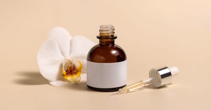 Brown glass dropper bottle near white orchid flowers on light yellow, close up, mockup. Skincare handmade beauty product, serum or lotion. Exotic natural cosmetics..