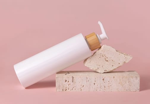 White one pump bottle lies on travertine stone on light pink, close up, mockup. Skincare beauty product. Natural cosmetics, lotion or cleanser. Minimal composition..