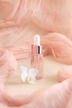 Light Pink Dropper Bottle near white orchid flower on light yellow, close up, mockup. Skincare beauty product, Aromatic oil or serum. Exotic cosmetics, pastel minimal composition..