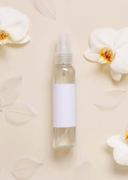 One pump dispenser bottle near white orchid flowers on light yellow top view, mockup. Skincare beauty product package. Exotic natural cosmetics, pastel minimal composition..