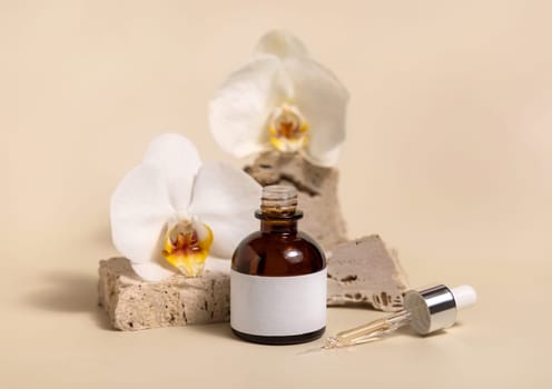 Brown glass dropper bottle on stone near white orchid flowers on light yellow, close up, mockup. Skincare handmade beauty product, serum or lotion. Exotic natural cosmetics..