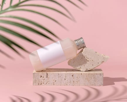 Cosmetic bottle with blank label lies on stone on light pink, palm leaf hard shadow , close up, mockup. Skincare beauty product. Natural cosmetics, lotion or cleanser..