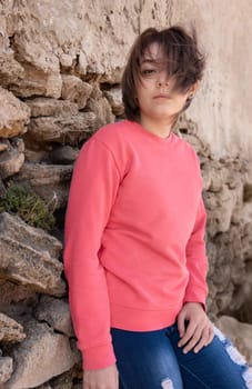 Teen girl wearing pink long sleeve shirt looking into a camera. Mockup. Serious Teenager girl standing outdoor near a wall, spending her time alone. Adolescence concept