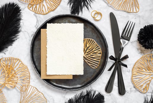 Black and golden wedding table setting with a place card and rings top view, mockup. Elegant flat lay with handmade paper card, wedding or holiday stationery template