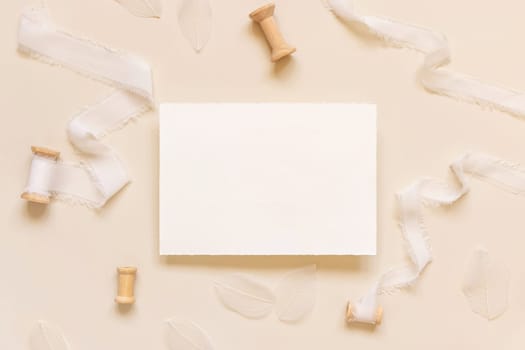 Wedding Card near white silk ribbons on light yellow top view, mockup. Romantic scene with horizontal blank card flat lay. Valentines or Spring romantic concept