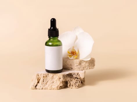 Green glass dropper bottle on stone near white orchid flower on light yellow, close up, mockup. Skincare handmade beauty product, serum or lotion. Exotic natural cosmetics..