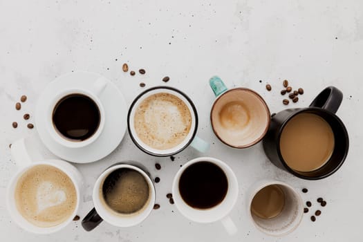 Top view on flat lay with many different full and empty coffee cups composition on gray white concrete background. Variety of tea mug collection layout. Dried coffee beans. Espresso, latte, americano