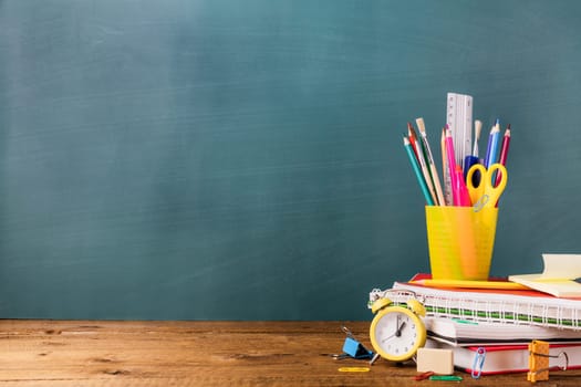 Many different various school, office supplies and stationery. Back to school concept. Notebook, book, pen, pencil, scissors, alarm clock, clock, sticker stand on a wooden table on a green background.