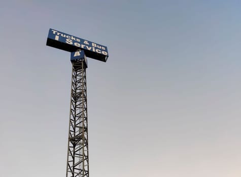 Trucks and bus service sign pole over blue sky.