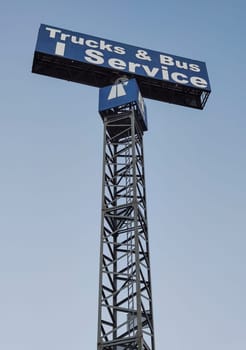 Trucks and bus service sign pole over blue sky.