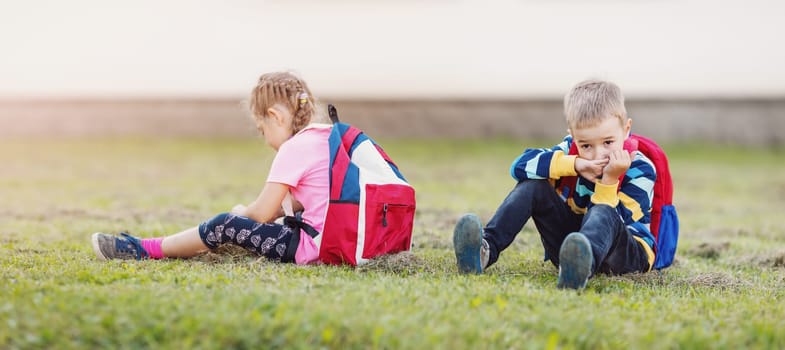 A boy and a girl quarreling and are sitting on the grass in the schoolyard back to back. Concept of friendship and back to school.