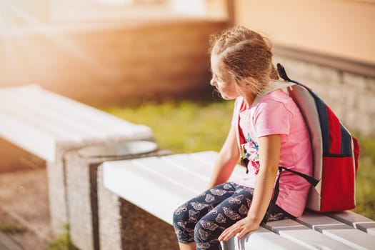 Schoolgirl sitting alone on the bench near the school. Concept of the back to school and studying.