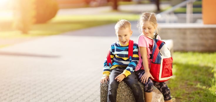 Boy and girl sitting on the stone near the school. Concept of back to school and friendship.