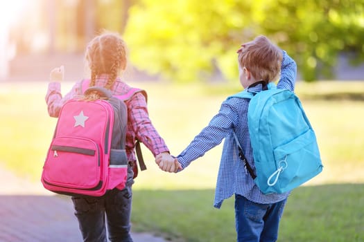 Girl and boy going to the school holding hands to study at it. Concept of back to school and friendship.