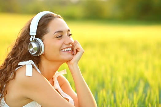 Happy woman listening to music with wireless headphones sitting in a wheat field