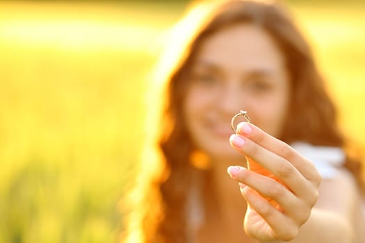 Close up portrait of a happy woman showing her engagement ring at sunset in a field