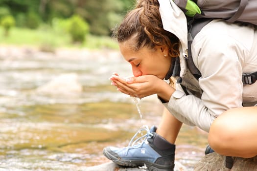 Profile of a trekker drinking water directly from river with cupped hands in the mountain