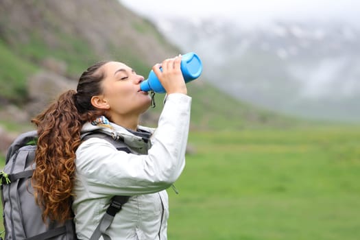 Trekker drinking water from canteen standing alone in the mountain a foggy day
