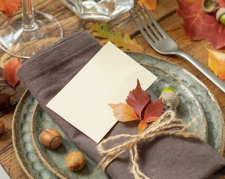 Autumn rustic table place with card between colorful leaves and berries, close up mockup. Blank card on wooden table, copy space. Thanksgiving or harvest concept