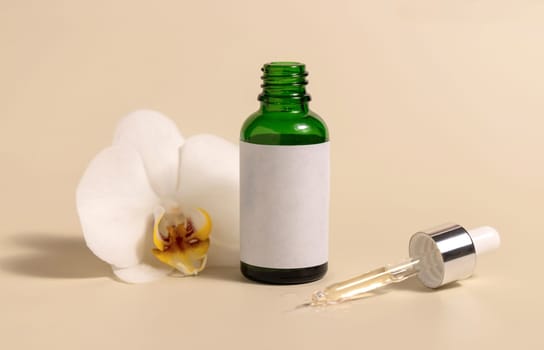 Green glass dropper bottle near white orchid flowers on light yellow, close up, mockup. Skincare handmade beauty product, serum or lotion. Exotic natural cosmetics..