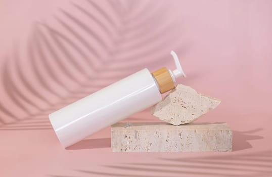 White one pump bottle lies on stone on light pink, palm leaf hard shadow behind, close up, mockup. Skincare beauty product. Natural cosmetics, lotion or cleanser. Minimal composition..