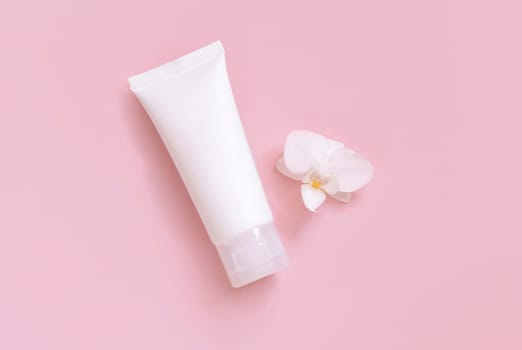 White plastic cream tube near white orchid flower on light yellow, top view, mockup. Skincare beauty product, cream or lotion. Exotic natural cosmetics, pastel minimal composition..