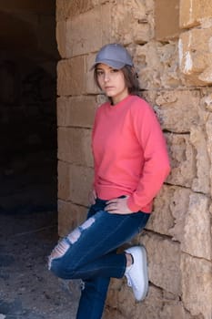 Teen girl wearing pink long sleeve shirt and baseball cap looking aside. Mockup. Serious Teenager girl standing outdoor near a wall, spending her time alone. Adolescence concept