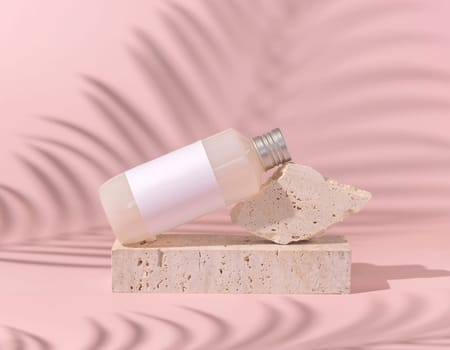 Cosmetic bottle with blank label lies on stone on light pink, palm leaf hard shadow behind, close up, mockup. Skincare beauty product. Natural cosmetics, lotion or cleanser..