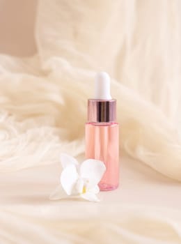 Light Pink Dropper Bottle near white orchid flower on light yellow, close up, mockup. Skincare beauty product, Aromatic oil or serum. Exotic cosmetics, pastel minimal composition..