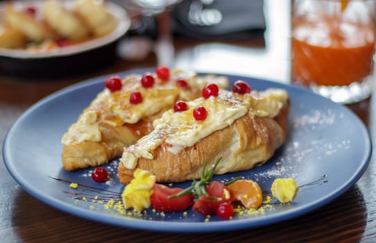 Freshly baked croissants with white, soft and sweet cream, red berries on a plate. Continental breakfast of two delicious croissants with cream on a dark wooden table in a restaurant