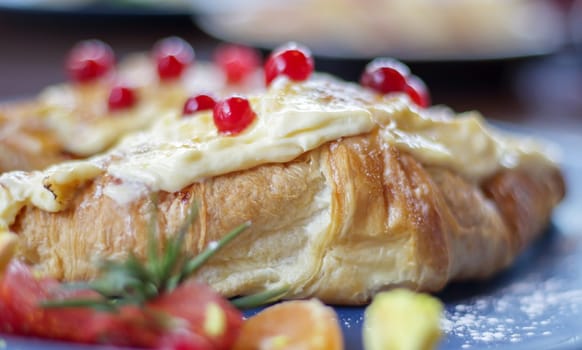Freshly baked croissants with white, soft and sweet cream, red berries on a plate. Continental breakfast of two delicious croissants with cream on a dark wooden table in a restaurant