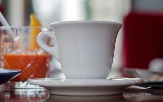 Hot coffee drink in a white cup on a wooden table on a blurred background of a cafe interior. Coffee drink with blurred cafeteria as background. Photo select focus