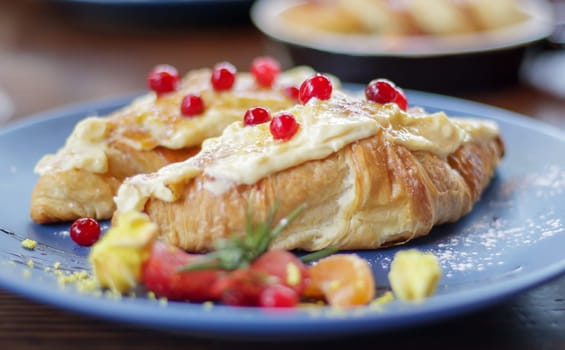 Freshly baked croissants with white, soft and sweet cream, red berries on a plate. Continental breakfast of two delicious croissants with cream on a dark wooden table in a restaurant