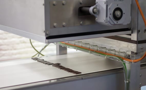 Production of sweets in a chocolate factory. Food industry plant. A male worker in uniform oversees the production process of an automated conveyor belt. Master factory worker
