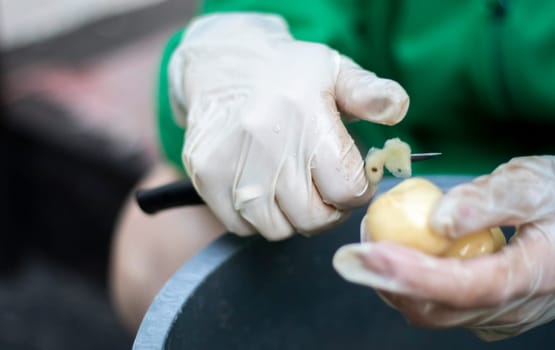 Woman's hands in white gloves peel raw new potatoes, close-up. Cleaning organic potatoes. Detail of female hands peeling fresh yellow potato with kitchen knife, food preparation concept