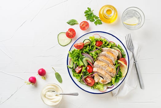 Healthy green salad with chicken breast and fresh vegetables on white table