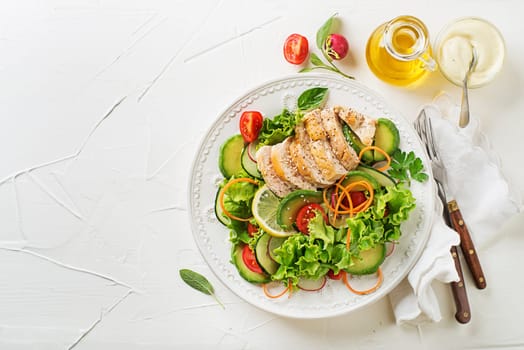 Healthy green salad with chicken breast and fresh vegetables on white table