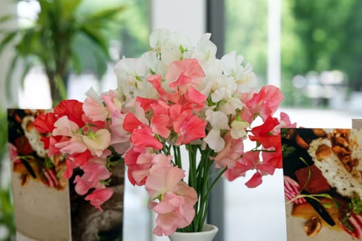 A bouquet of sweet peas in white and pink shades on a table in a cafe next to the menu