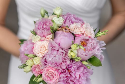 Bride's bouquet Beautiful of pink wedding flowers in the hands of the bride and rings on a pink bud