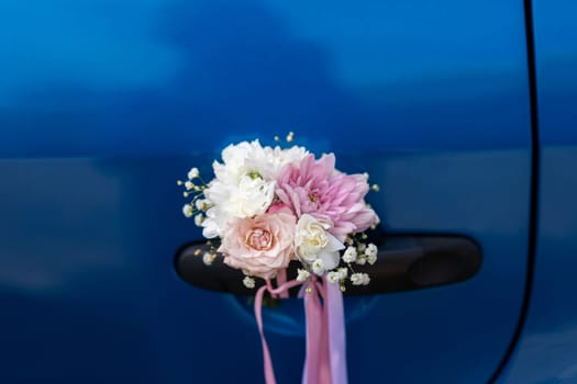 Wedding boutonniere on the handle of a blue car. Designer floral decoration.