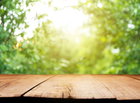 Empty wooden plank or deck, table top with background of blurred green trees, garden with sunlight or blurred foliage backyard. Nature with bokeh light. Mock up, template for product display, montage