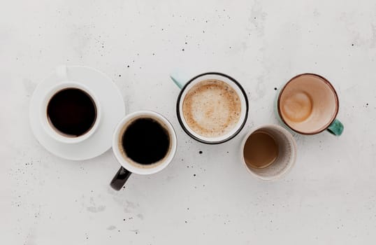 Top view on flat lay with many different full and empty coffee cups composition on gray white concrete background. Variety of tea mug collection layout. Dried coffee beans. Espresso, latte, americano