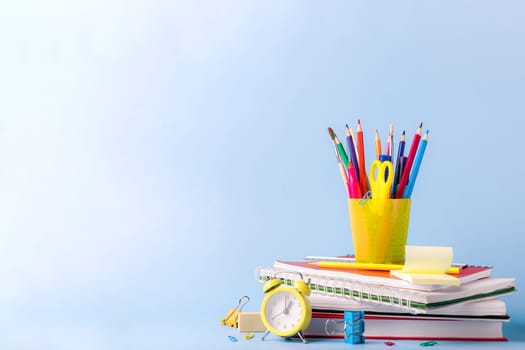 Many different various school, office supplies and stationery. Back to school concept. Notebook, book, pen, pencil, scissors, alarm clock, clock, sticker stand on a wooden table on a green background.