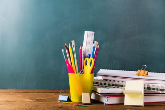 Many different various school, office supplies and stationery. Back to school concept. Notebook, book, pen, pencil, scissors, alarm clock, clock, sticker stand on a wooden table on a green background.
