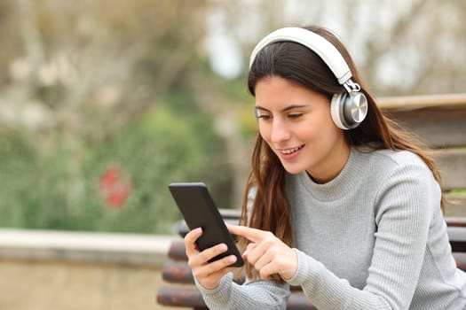 Happy teen using smart phone listening to music with headphones in a park