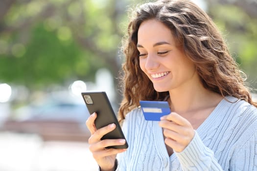 Happy woman buying online with credit card and cell phone in the street