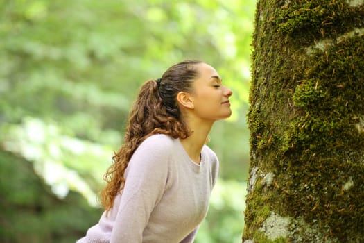 Profile of a happy woman smelling moss in a tree in a forest